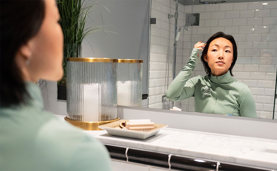 En kvinde som speljer sig i spejlet i et badeværelse. En kvinde som speljer sig i spejlet i et badeværelse.