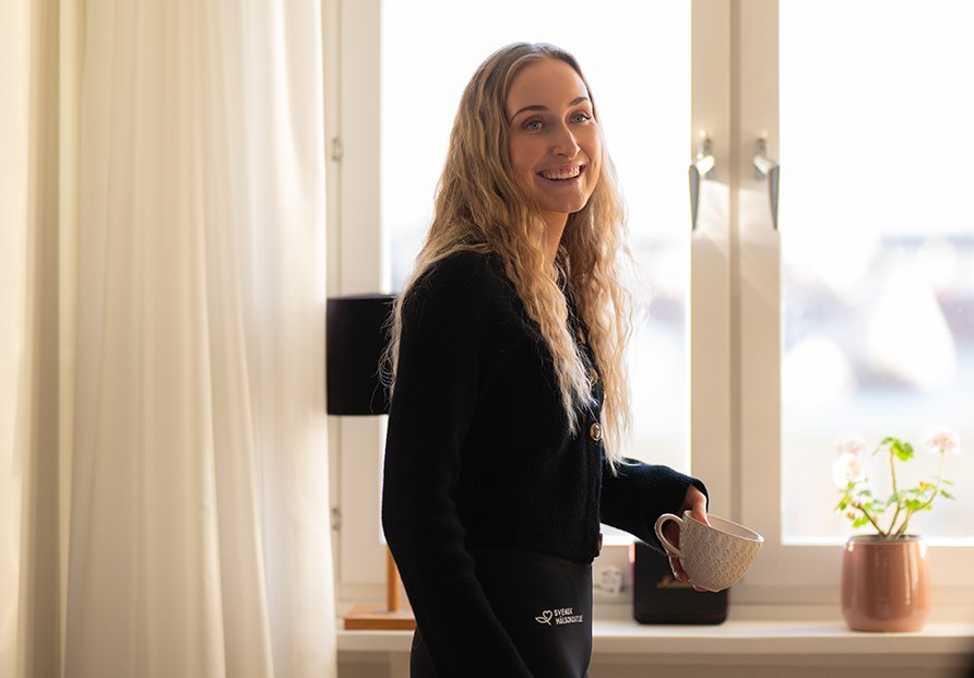 Annie ved vinduet med en kop i hnden.