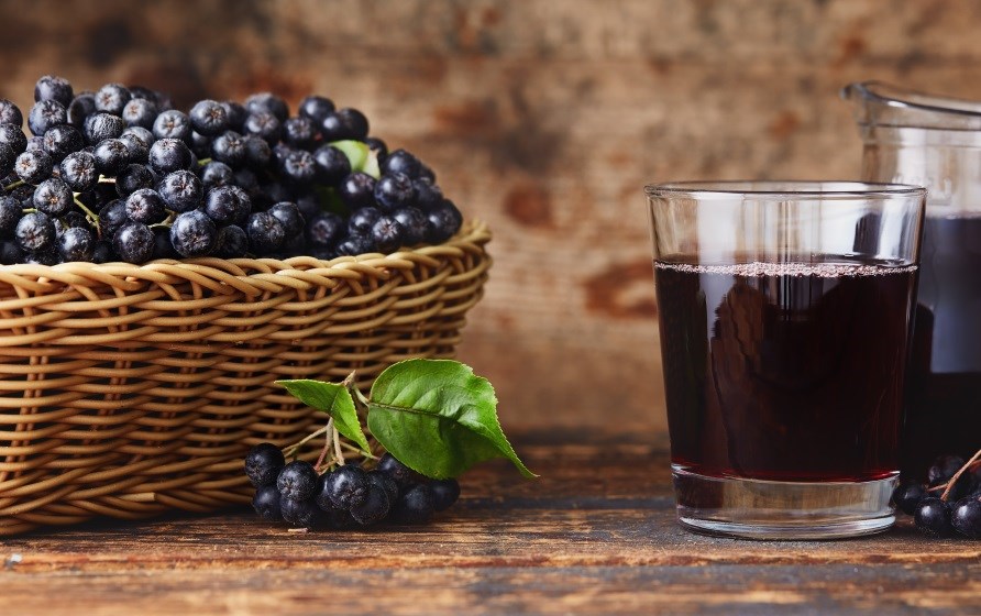 En kurv fyldt med aronia bær står på et træbord, ved siden af et glas aronia juice. En kurv fyldt med aronia bær står på et træbord, ved siden af et glas aronia juice.