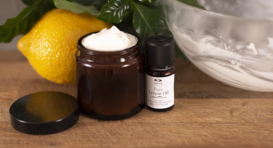 Hjemmelavet body butter i en brun glaskrukke med en citron og pure lemon oil ved siden af.