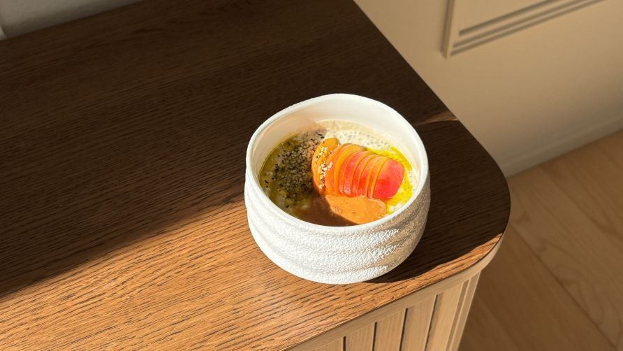 En sk�l med chiabudding toppet med ferskner, mandelsm�r, hampf�r og avokadoolie st�r p� en kommode.