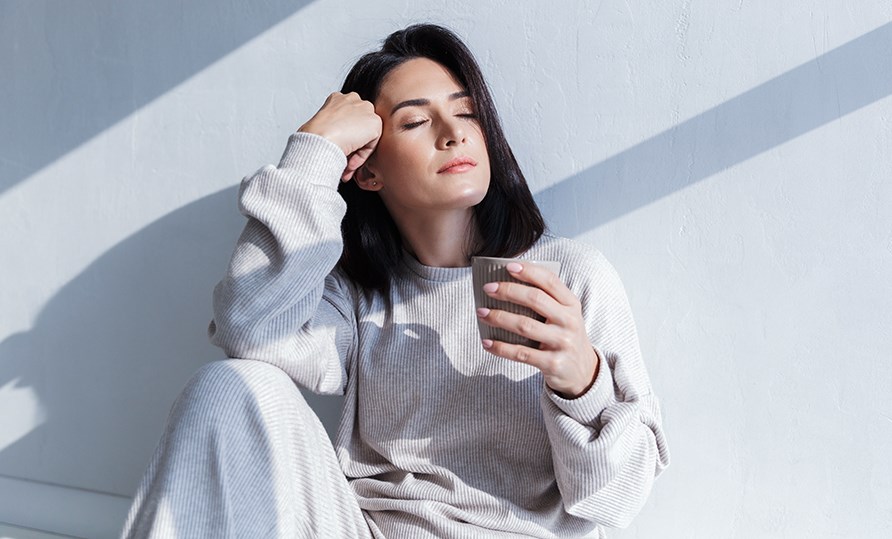 En kvinde sidder udmattet op af en mur med en kop og hviler hovedet på hendes hånd. En kvinde sidder udmattet op af en mur med en kop og hviler hovedet på hendes hånd.