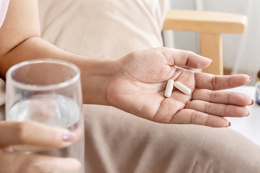 En kvinde, der holder to kapsler i den ene hnd og et glas vand i den anden. 