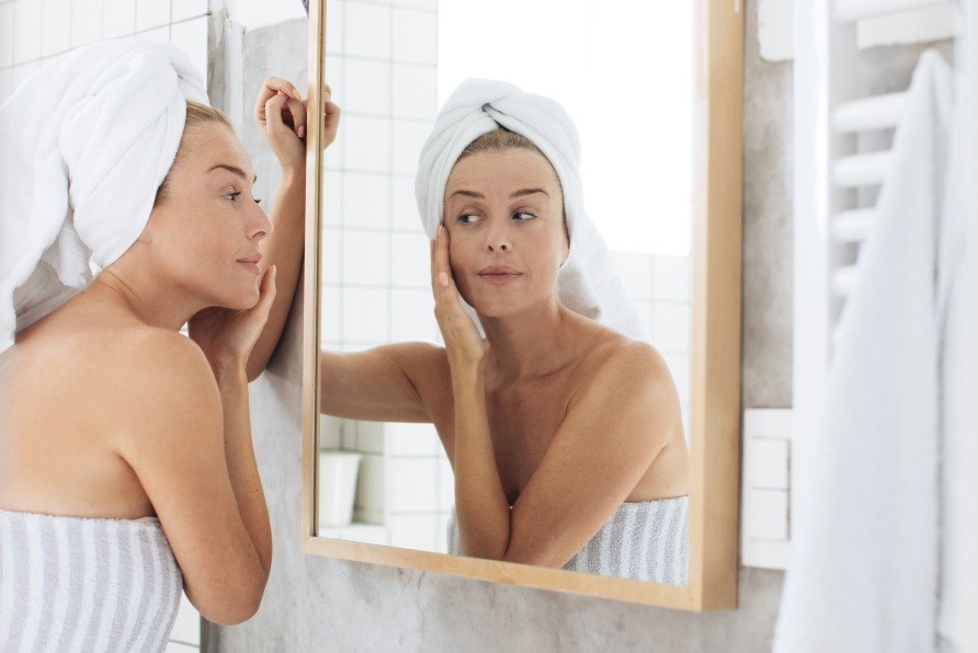 Kvinde i badevrelse smrer ansigtet ind i creme.