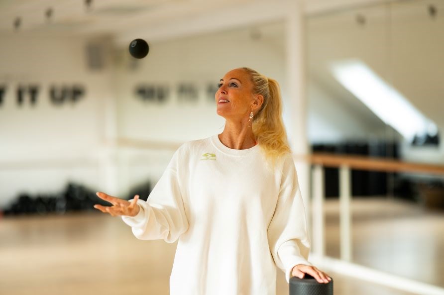 Gitte Salling str i en trningssal, hvor hun smider en bold op i luften.