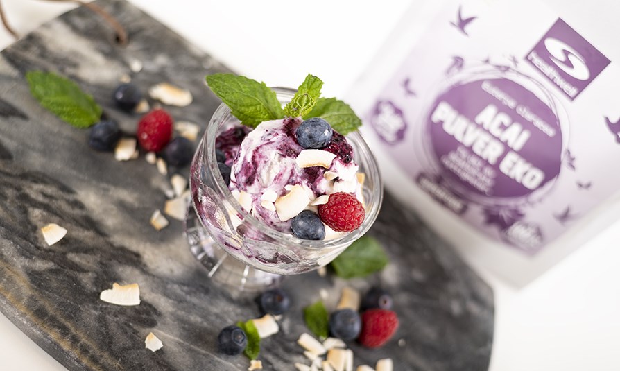 A�a�-is i et glas servet med koskosflager, b�r og mynte, p� et bord.