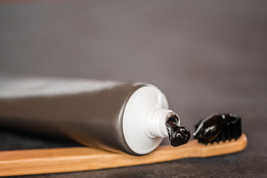 Tandpastatube med aktivt kul, lidt tandpasta trykket ud på en tandbørste bag tuben. Tandpastatube med aktivt kul, lidt tandpasta trykket ud på en tandbørste bag tuben.