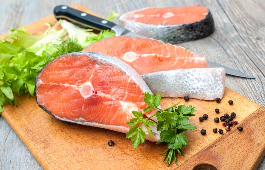 Tre laksekoteletter p et skrebrt med en kniv, salatblade og urter.