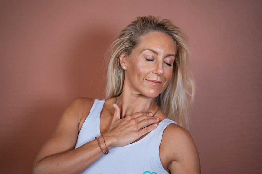 Johanna Hector str foran en rosa vg og giver hende selv en lymfemassage ved halsen.