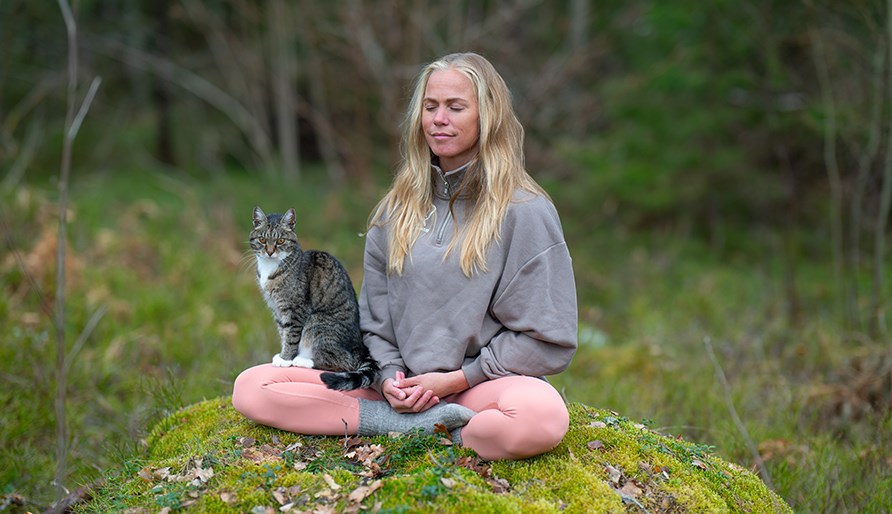 Josefine sidder p en sten og mediterer med en kat i skdet.