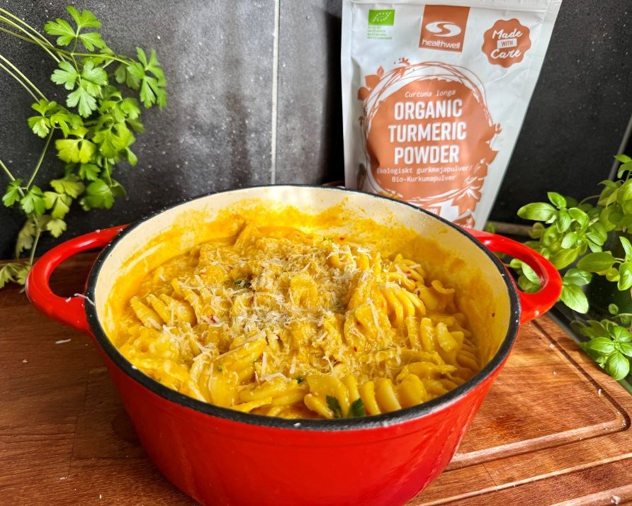 Kalorismarts kyllingegryde i en stor, r�d gryde p� en k�kkenb�nk af tr�, og en pakning med Healthwell Gurkemeje Pulver �KO.