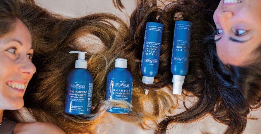 To smilende kvinder, der ligger ned og kigger p� hinanden med deres h�r spredt ud mellem dem. P� h�ret ligger flasker med h�rplejeprodukter.