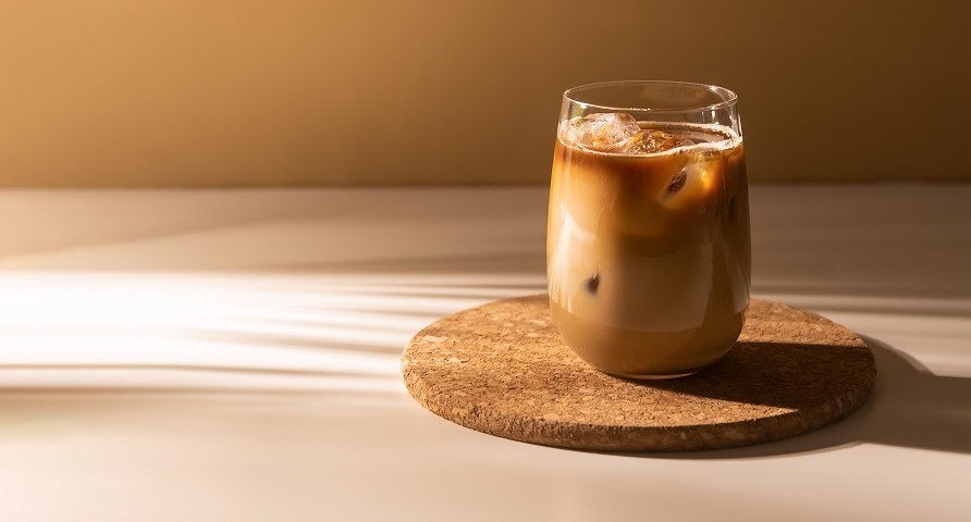 Et glas med proffee str p en kork bordskner med en brunlig baggrund.