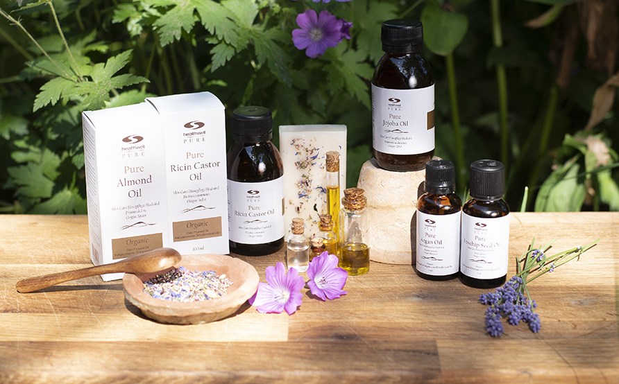 Flere flasker med naturlige og vegetabilske oljer som str p et bord ude i naturen.