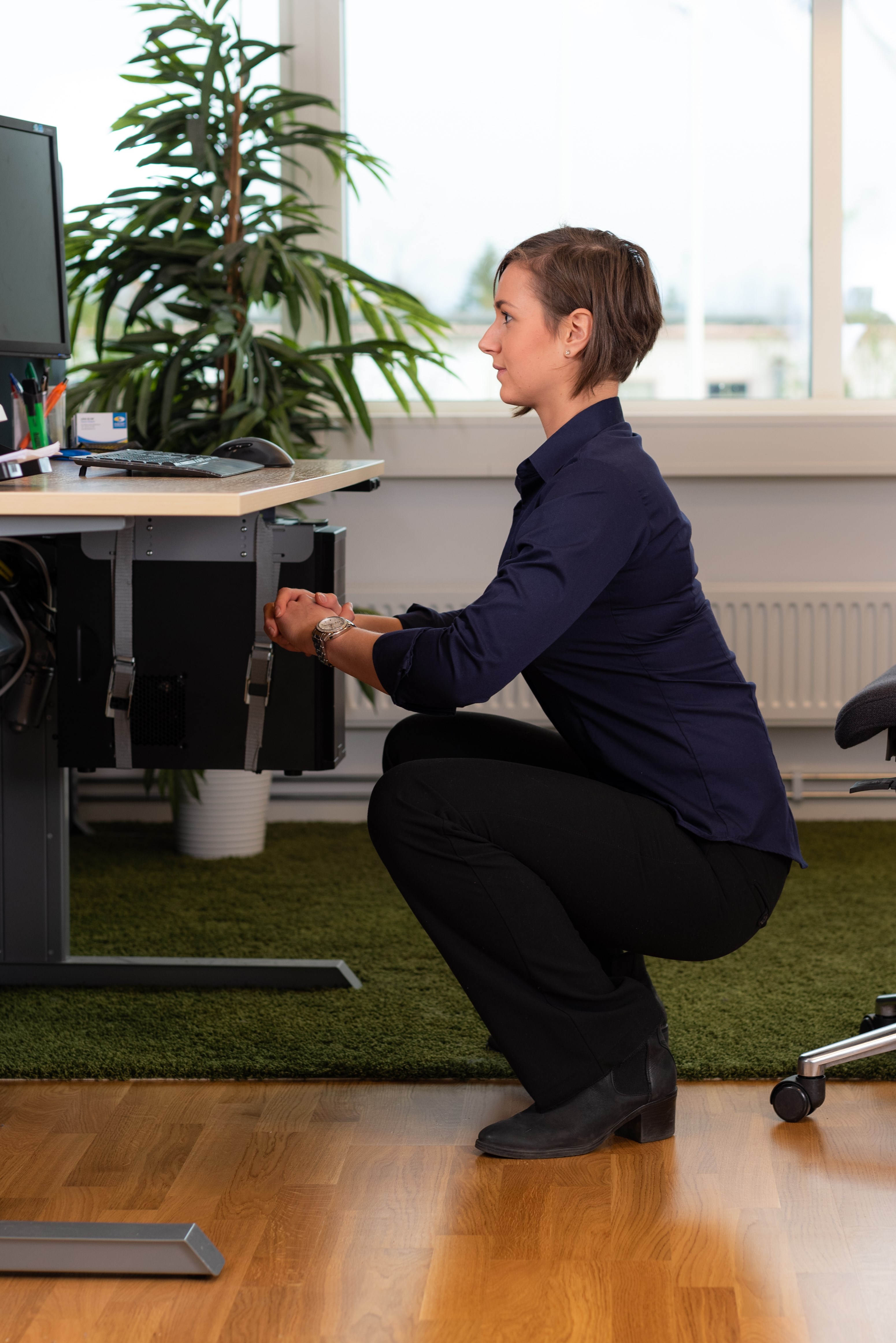 En kontorklædt kvinde sidder på hug med ret ryg foran sit skrivebord. En kontorklædt kvinde sidder på hug med ret ryg foran sit skrivebord.