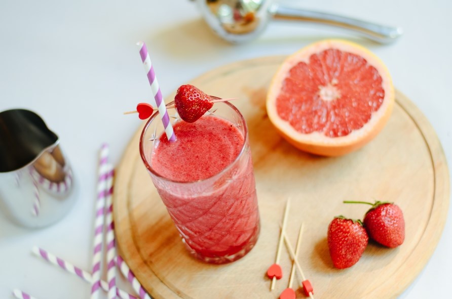 Et glas med juice str p et bord sammen med grapefrugt og jordbr.