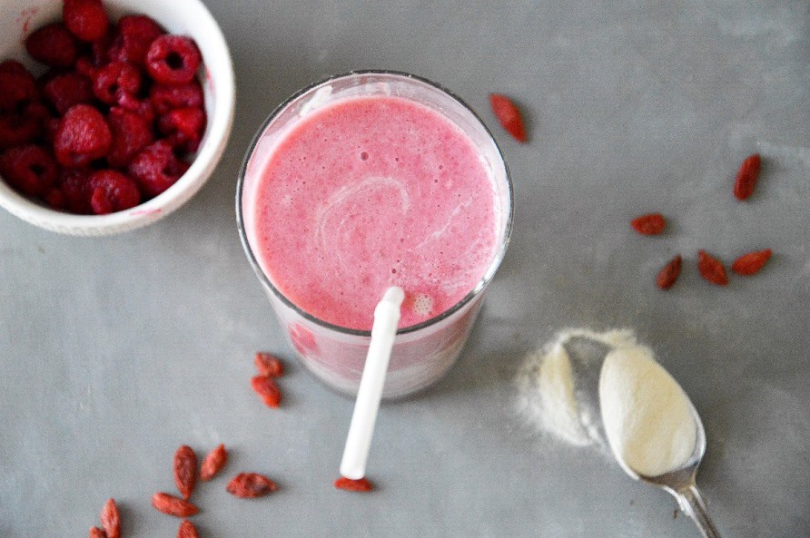 Et glas med en lyserd smoothie med br p et bord.