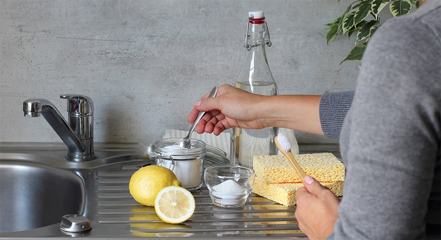 Billede af en arm, der holder en teske i en gennemsigtig sk�l med natron, p� en k�kkenbord.